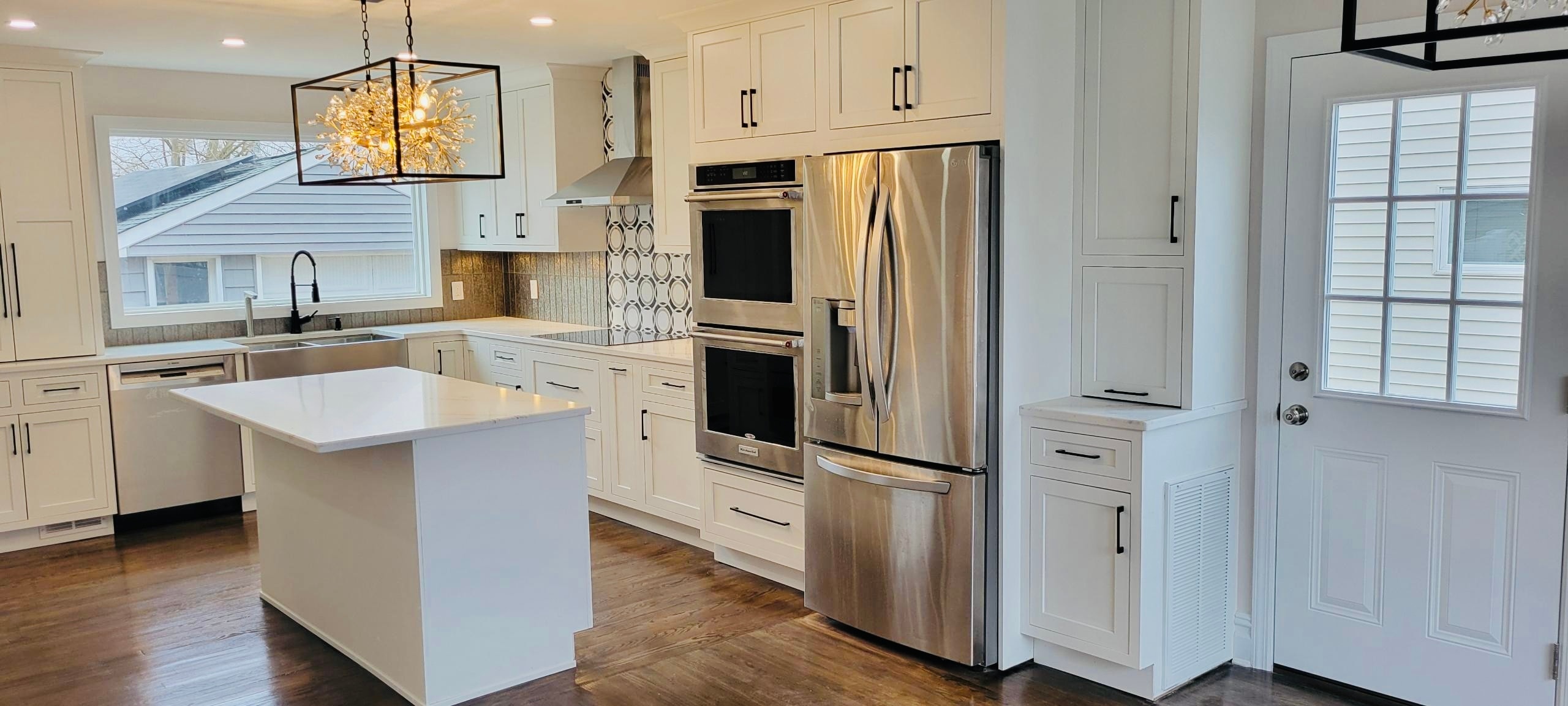 Kitchen renovation with white shaker cabinets, stainless double oven and statement chandelier